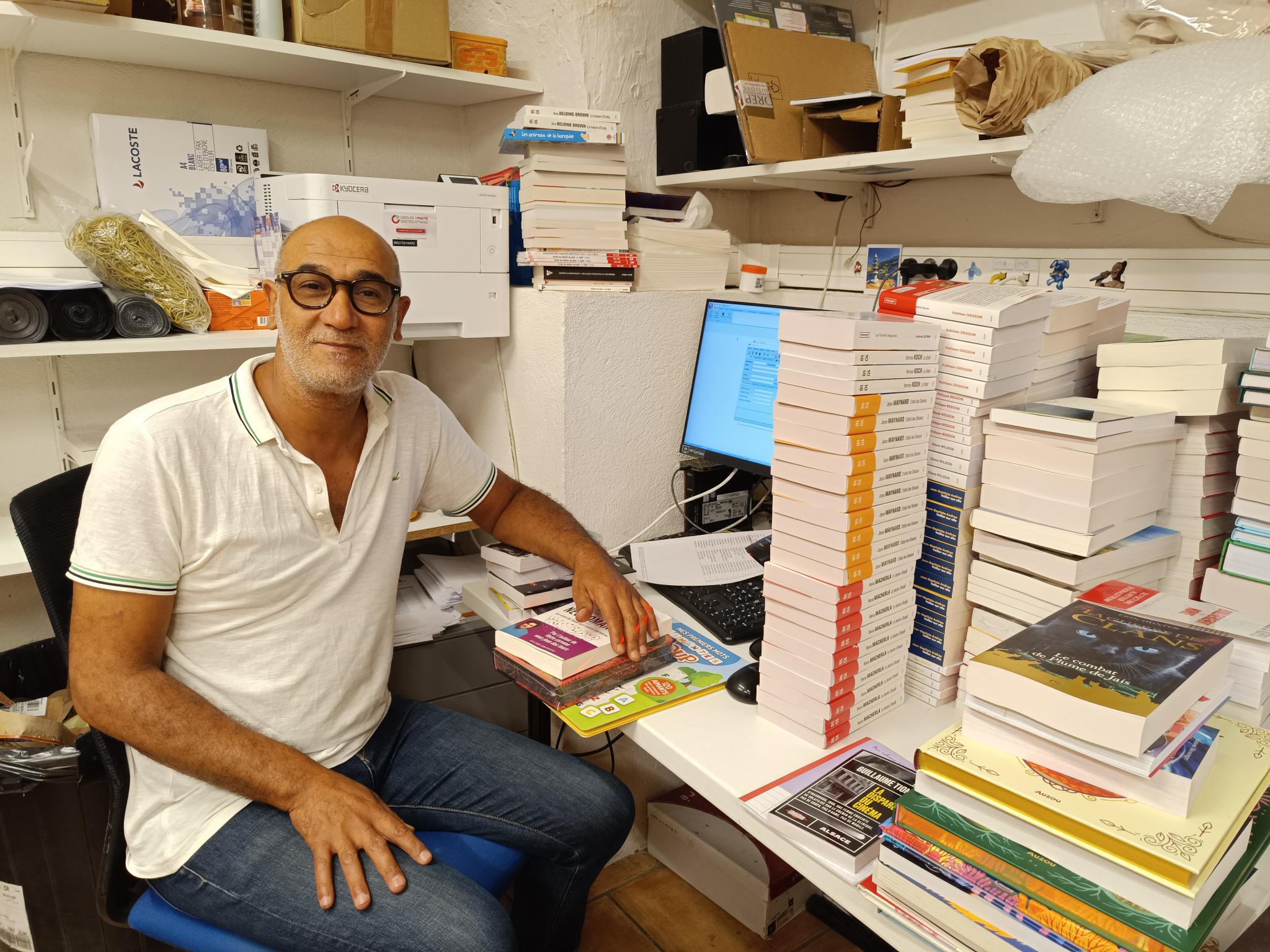 Messaoud Azzouz, un des réceptionnaires de la librairie Goulard, assis à son bureau et entouré de livres.