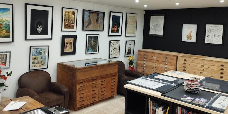 La galerie de la librairie Nicolas Sanchez avec des fauteuils et une grande table pour admirer les oeuvres présentes.