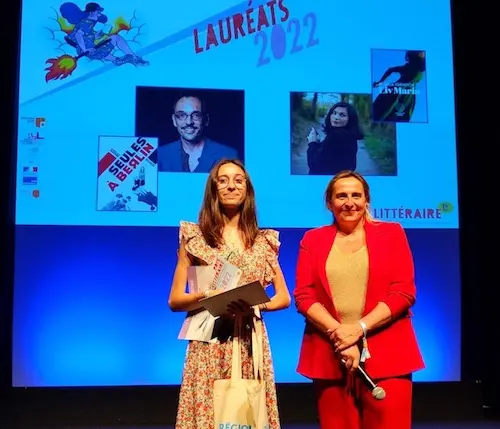 Deux femmes sont debout sur une scène, l'une d'elles tient un trophée dans ses mains.