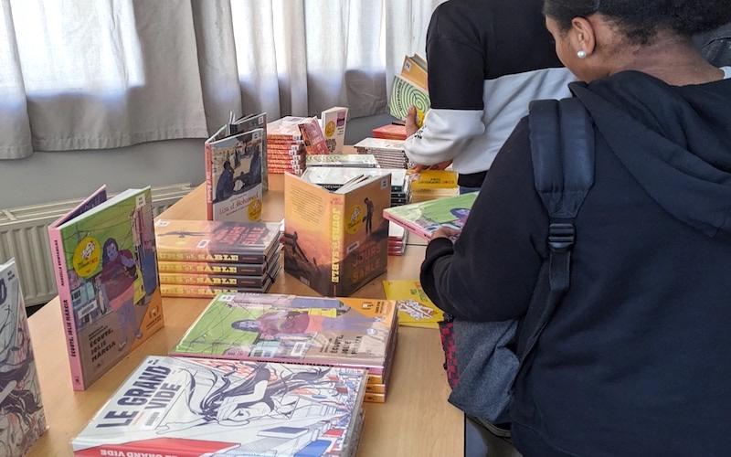 Deux adolescents regardent des romans et des bandes dessinées disposés sur une table.